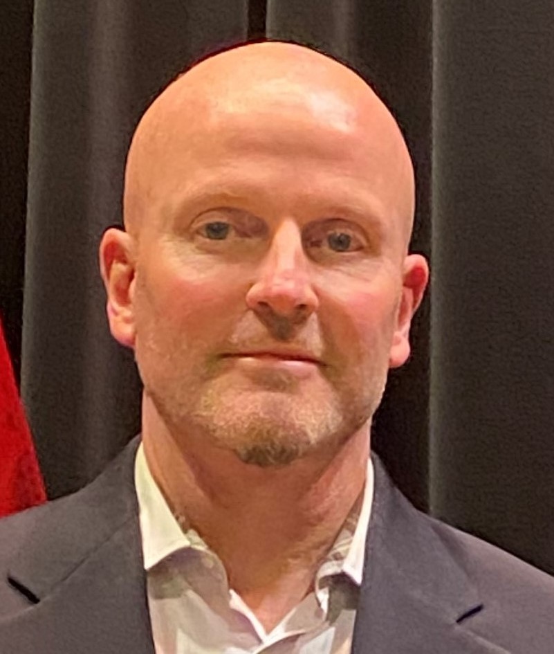 a smiling bald man wearing a colored shirt and sport jacket