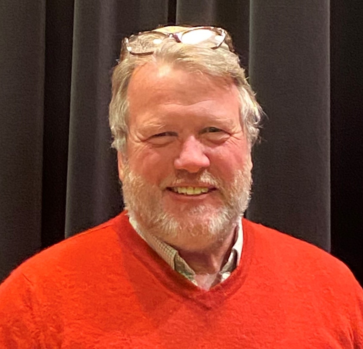 a smiling man with a beard wears a red sweater 