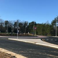 blue sky and leafless trees are seen in the background with a road leading towards a traffic circle in the foreground. 