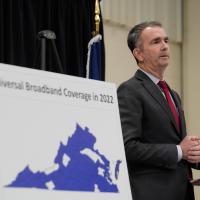 Virginia Governor Ralph Northam stands beside a map of Virginia displaying broadband coverage areas. 