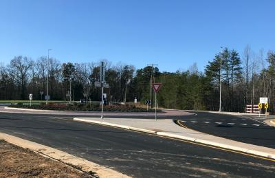 blue sky and leafless trees are seen in the background with a road leading towards a traffic circle in the foreground. 