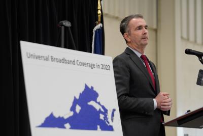 Virginia Governor Ralph Northam stands beside a map of Virginia displaying broadband coverage areas. 