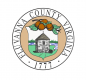 the County Seal depicting a small stone building in a green field, with persimmon fruit hanging from border of seal 